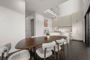 A modern kitchen with white cabinets, a dark wooden dining table, and grey upholstered chairs. - Stylish 3BR Snowy Mountains Getaway w/ Ducted A/C! (Jindabyne)