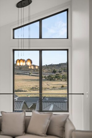 Ein Zimmer mit großem Fenster und Blick auf eine Landschaft, einer Deckenleuchte und einem Sofa mit Kissen.