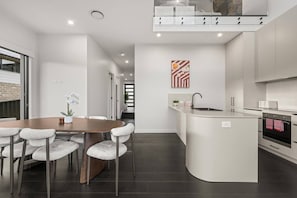 A modern kitchen with a central island, a dining area with a round table and chairs, and a staircase leading to an upper level. - Stylish 3BR Snowy Mountains Getaway w/ Ducted A/C! (Jindabyne)
