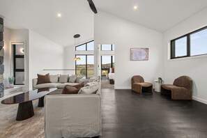 A spacious living room with a sectional sofa, a coffee table, and two armchairs. There is a large window providing a view of the outdoors. - Stylish 3BR Snowy Mountains Getaway w/ Ducted A/C! (Jindabyne)