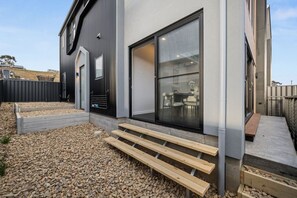 Een modern huis met een groot raam, een houten terras en een metalen hek.