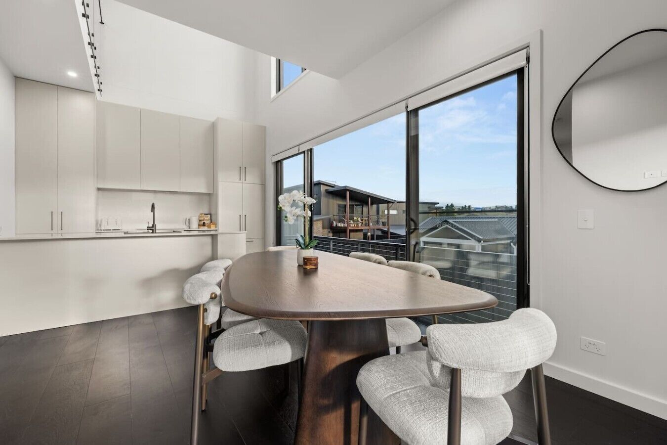A modern kitchen with white cabinets, a round dining table with six chairs, and a large window offering a view of a residential building.