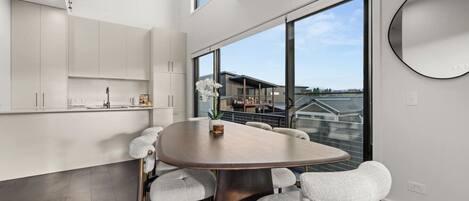 A modern kitchen with white cabinets, a round dining table with six chairs, and a large window offering a view of a residential building.