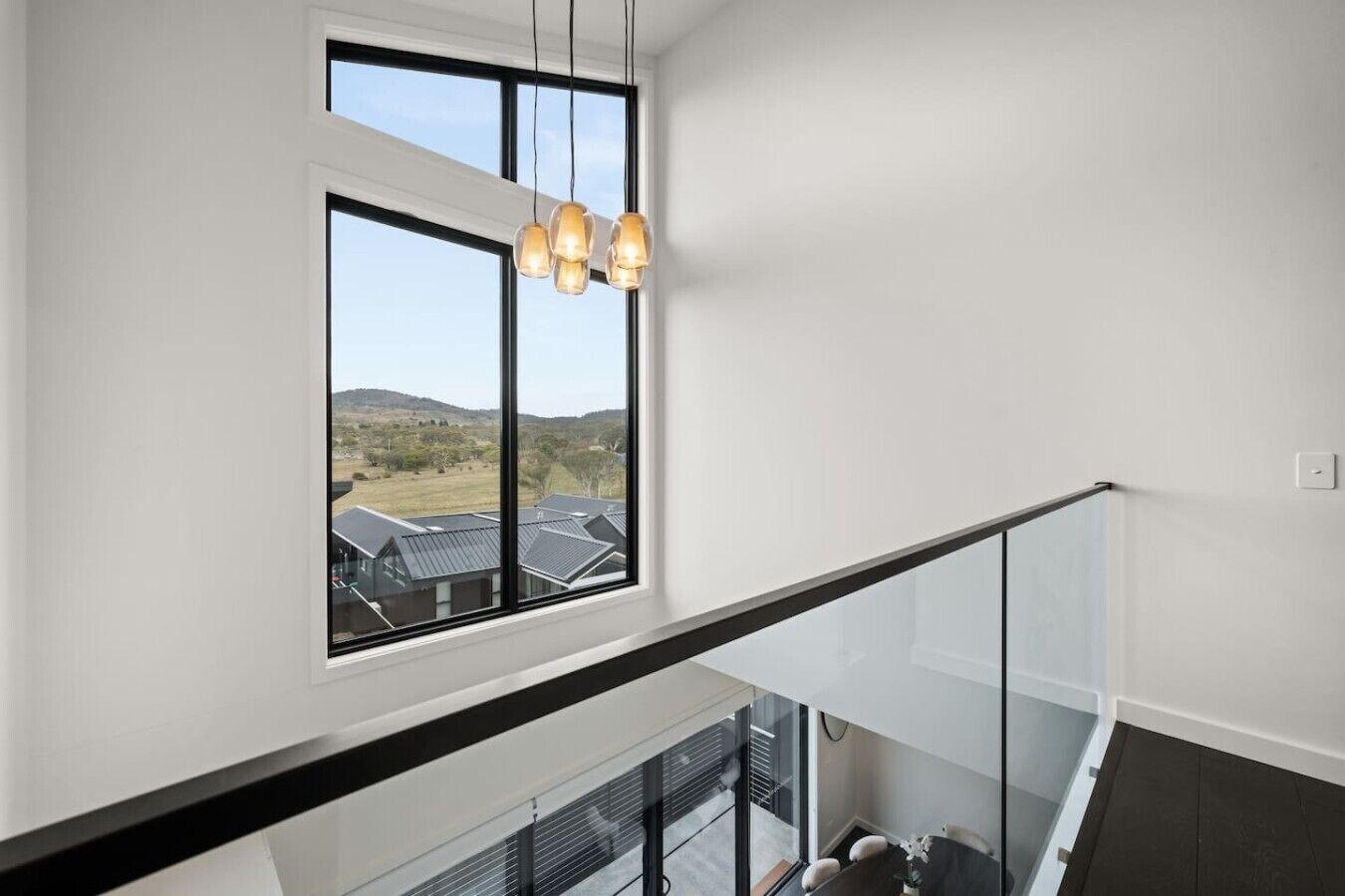 Een modern interieur met een groot raam, een glazen balustrade en uitzicht op huizen.