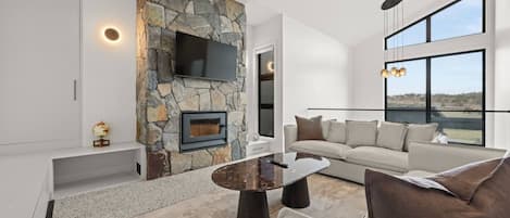 Una sala de estar moderna con chimenea de piedra, televisor de pantalla plana, sofá y ventanas amplias que ofrecen una vista.