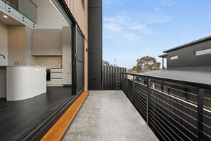 A modern kitchen with a curved island, a dining area with a black railing, and a view of the surrounding landscape. - Cozy Alpine Retreat | Fireplace & Mountain Charm (Jindabyne)