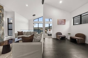 A spacious living area with a sofa set, a coffee table, and a dining table. There is a view of a bedroom through an open doorway. - Cozy Alpine Retreat | Fireplace & Mountain Charm (Jindabyne)