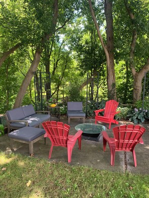 An outdoor seating area with red Adirondack chairs, a grey sofa, and a glass table.