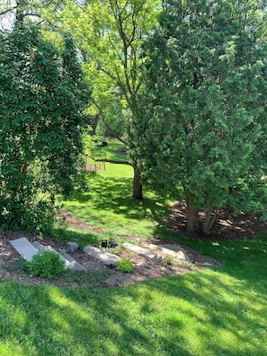 A well-maintained garden with a variety of trees, a stone pathway, and a grassy area.