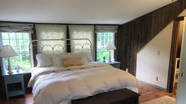 A bedroom with a bed, bedside tables, a bench, and a window. - Historic VT Retreat | Hot Tub, Views, Near Skiing (Mount Holly)