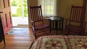 A room with a bed, two wooden chairs, a small table, a window with curtains, and a door leading to an outdoor area. - Historic VT Retreat | Hot Tub, Views, Near Skiing (Mount Holly)