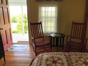 A room with a bed, two wooden chairs, a small table, a window with curtains, and a door leading to an outdoor area. - Historic VT Retreat | Hot Tub, Views, Near Skiing (Mount Holly)