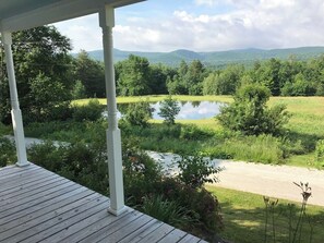 A wooden deck with a view of a lake and surrounding greenery. - Historic VT Retreat | Hot Tub, Views, Near Skiing (Mount Holly)