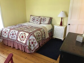 A bedroom with a bed, a nightstand, a lamp, and a small table. - Historic VT Retreat | Hot Tub, Views, Near Skiing (Mount Holly)