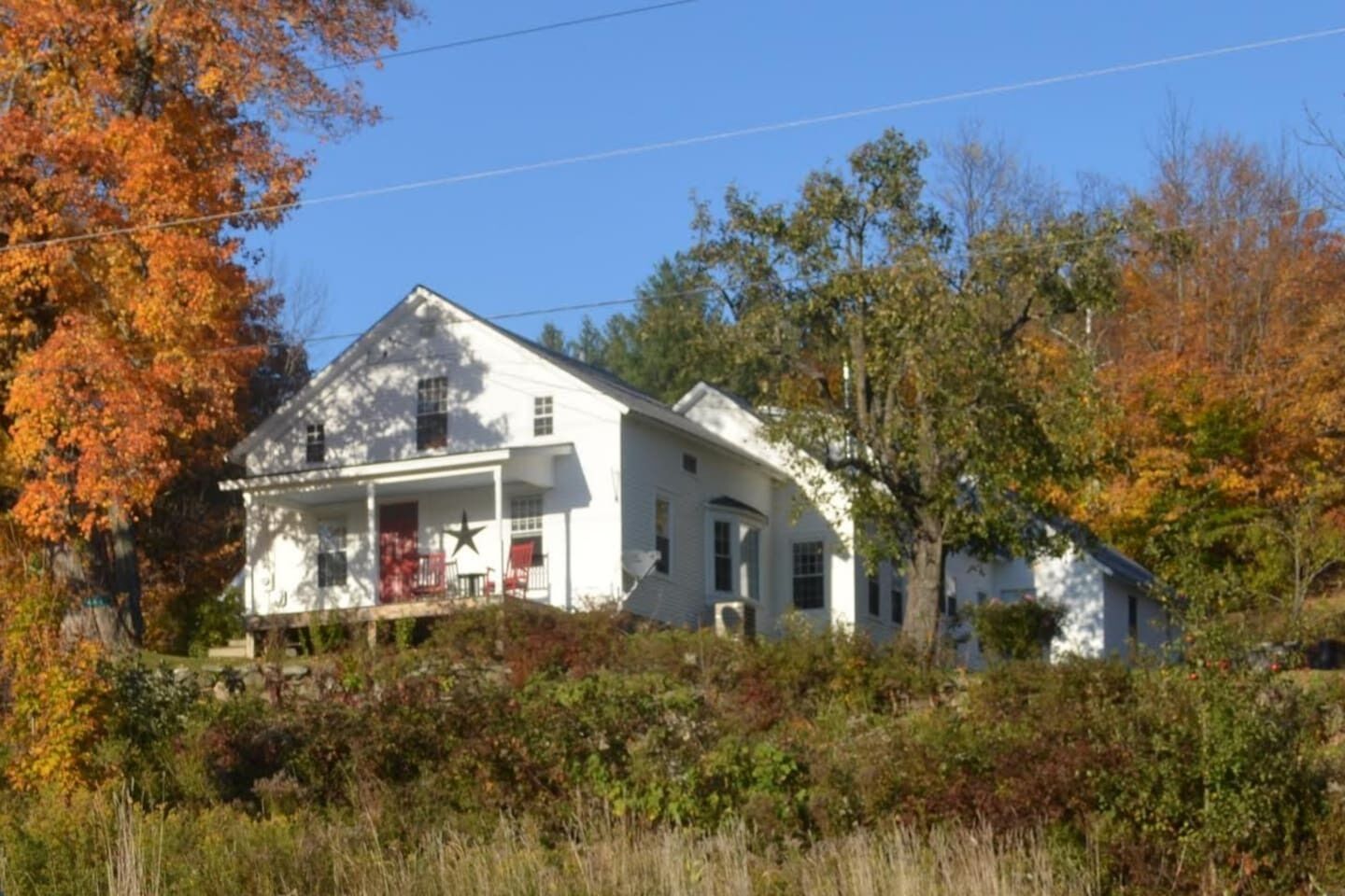 A white two-story house with a porch, surrounded by trees with autumn foliage.