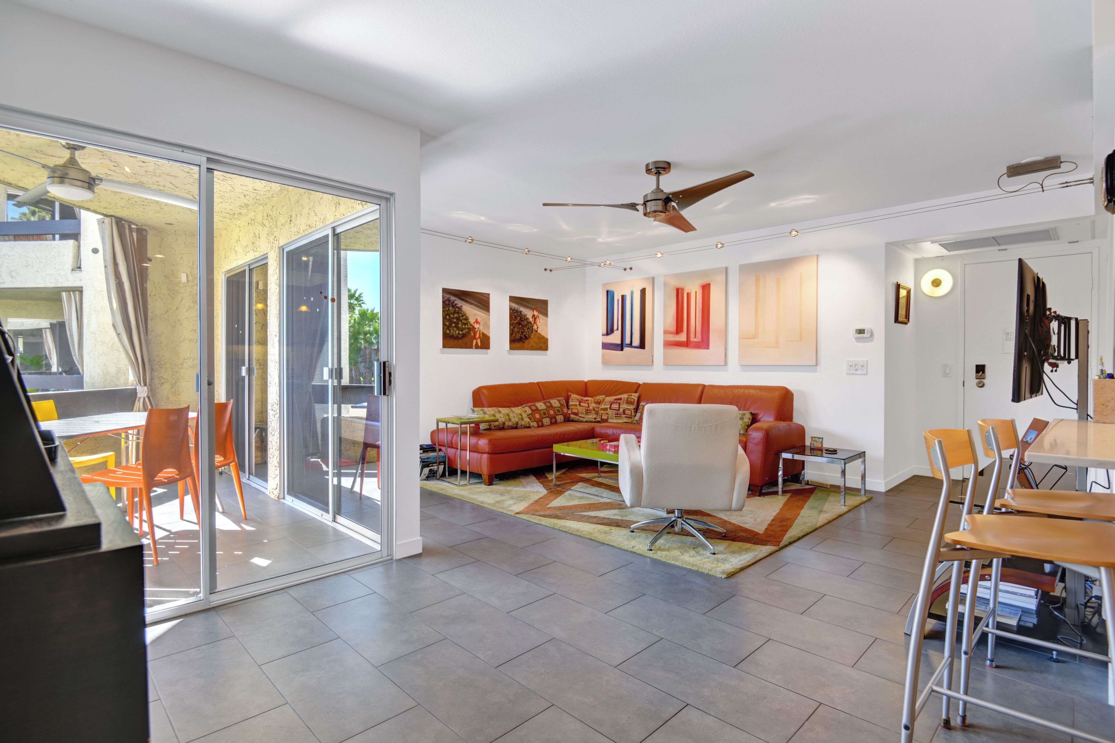 A modern living room with a glass door leading to a balcony, a red sofa, a white armchair, and a dining area with a table and chairs.