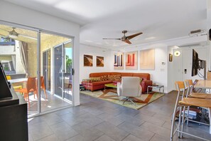 A modern living room with a glass door leading to a balcony, a red sofa, a white armchair, and a dining area with a table and chairs. - Stylish and fun second floor condo in exciting Palm Springs! (Palm Springs)