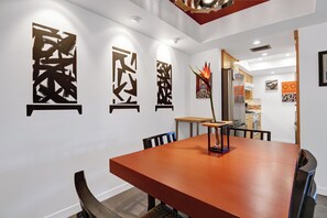 A modern dining area with a wooden table and chairs, a decorative plant, and abstract wall art. - Stylish and fun second floor condo in exciting Palm Springs! (Palm Springs)