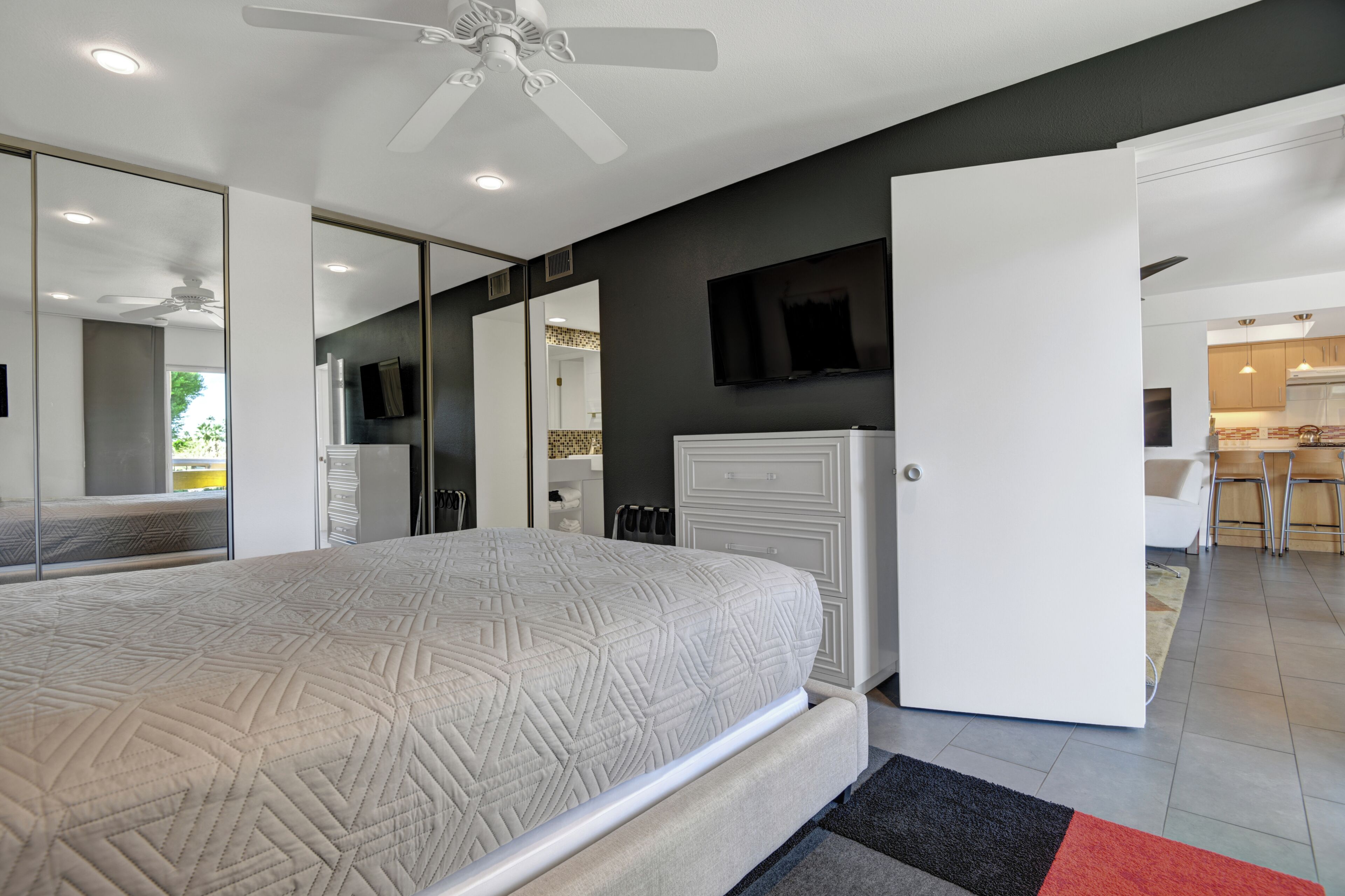 Un dormitorio moderno con una cama, un armario, un televisor y un baño visible a través de una puerta abierta.
