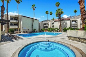 A swimming pool with lounge chairs, palm trees, and a building with balconies. - Stylish and fun second floor condo in exciting Palm Springs! (Palm Springs)
