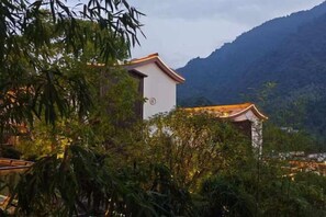 Un edificio tradicional con tejado de tejas, rodeado de vegetación exuberante y un paisaje montañoso al fondo.