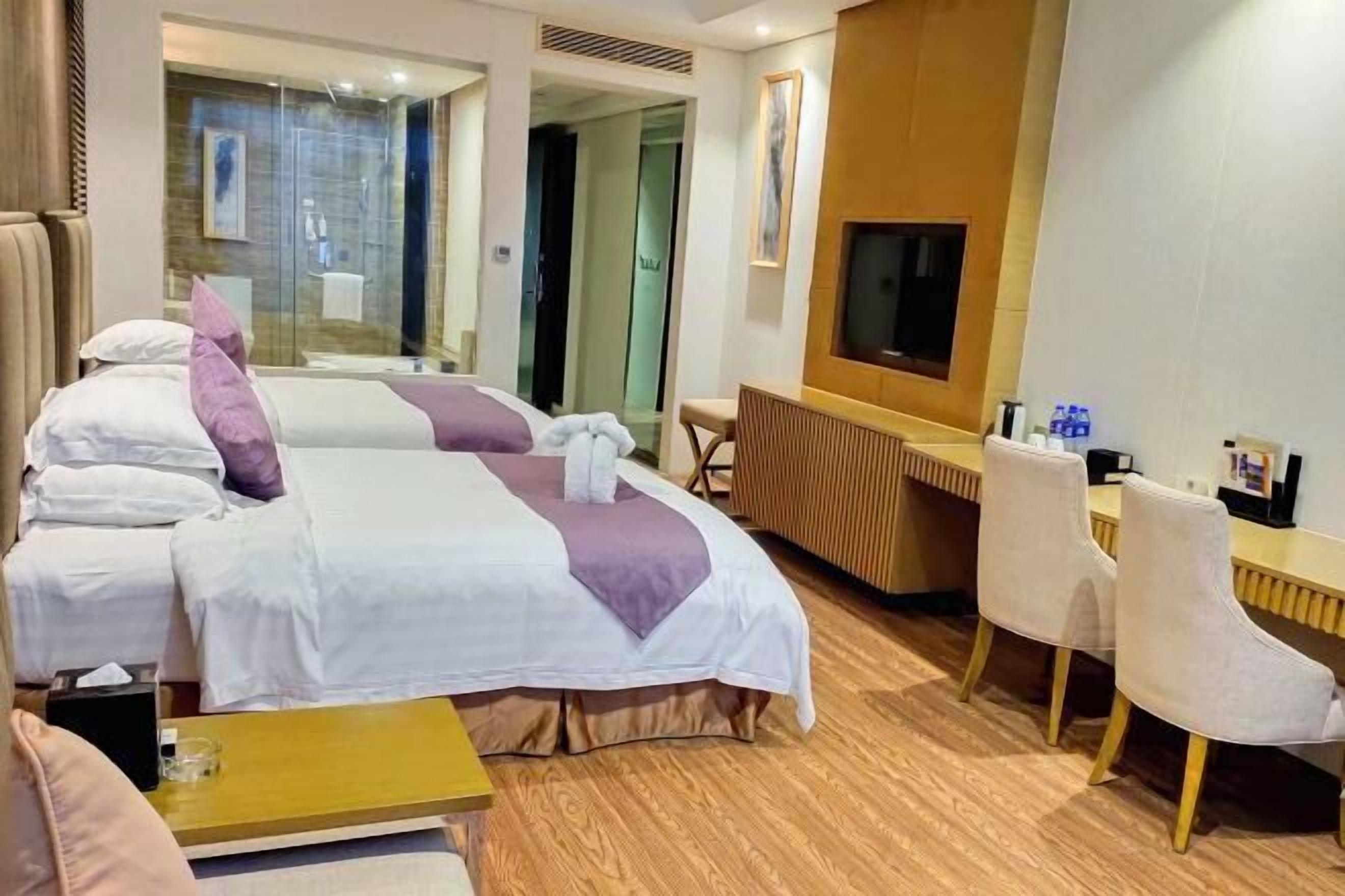 A hotel room with two beds, a desk, a TV, and a seating area.