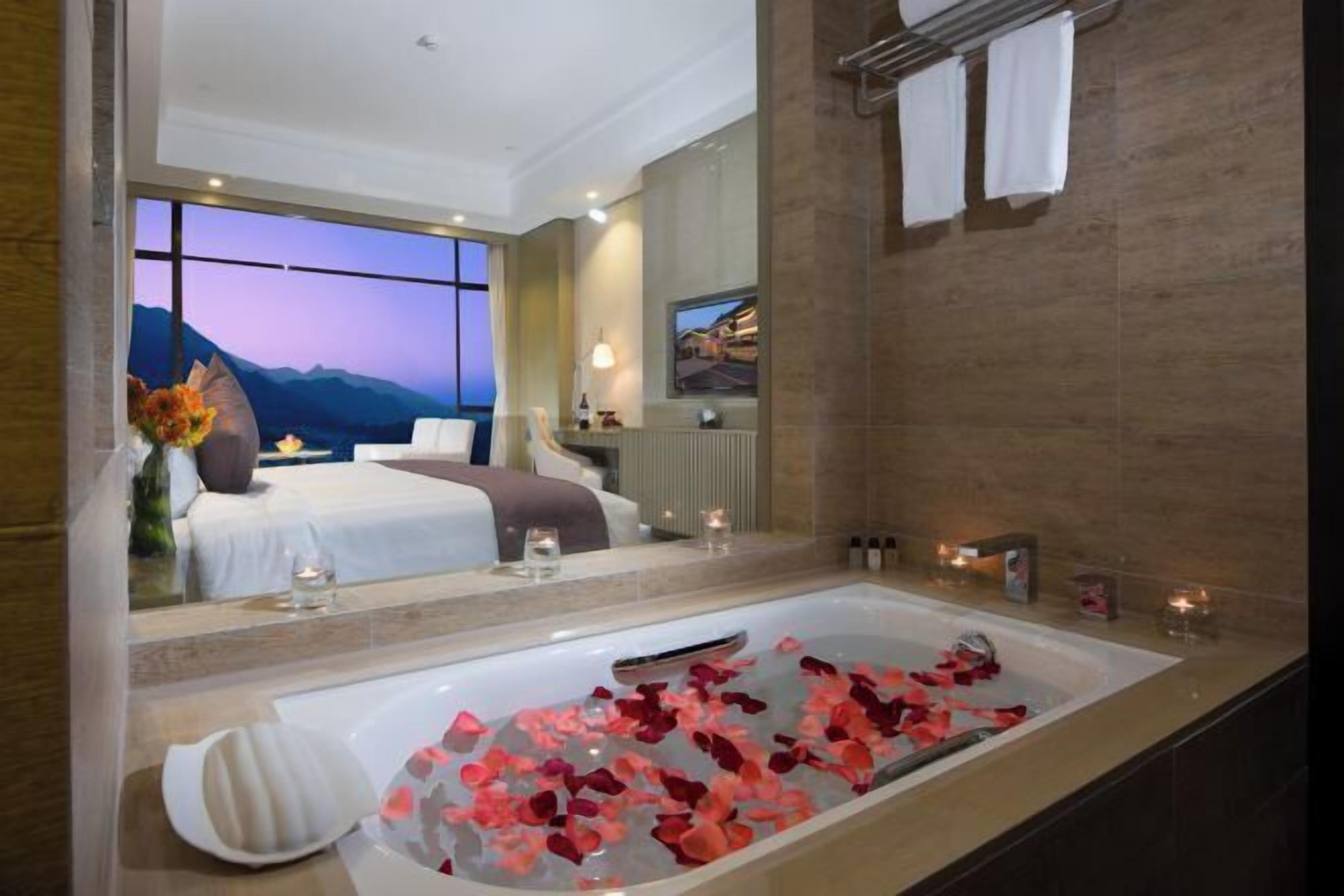 A modern hotel bathroom with a large bathtub, a mirror, and a view of the room.