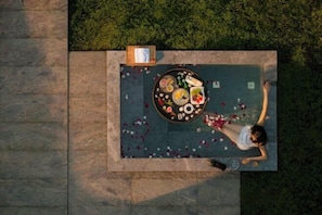 An aerial view of a rooftop terrace with a dining table, chairs, and scattered rose petals.