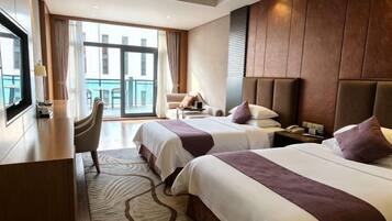 A hotel room with two beds, a desk, a chair, and a balcony view.