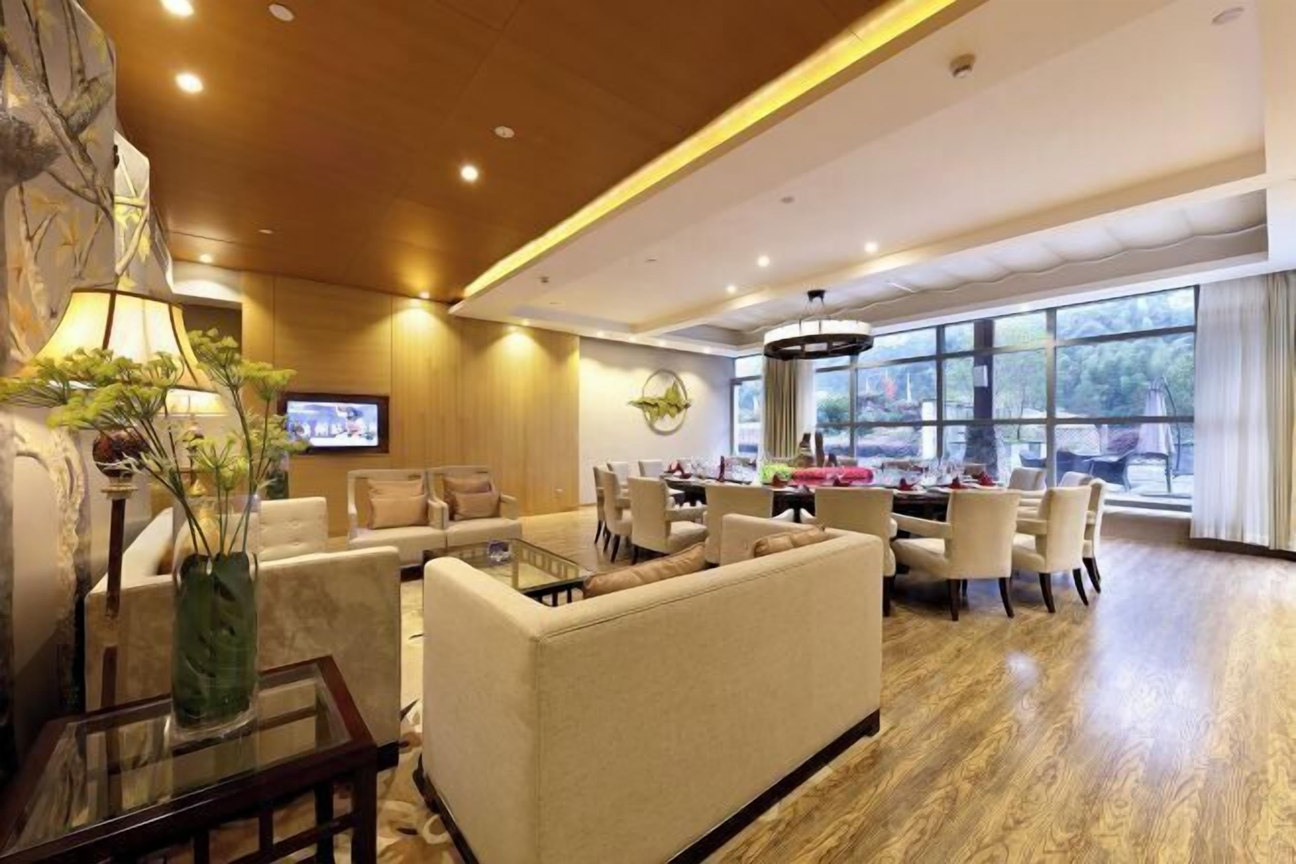 A hotel lobby with a sofa, dining table, chairs, a TV, and a large window.