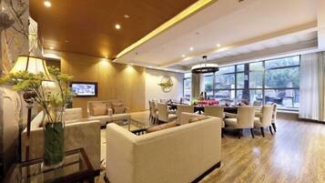 A hotel lobby with a sofa, dining table, chairs, a TV, and a large window.
