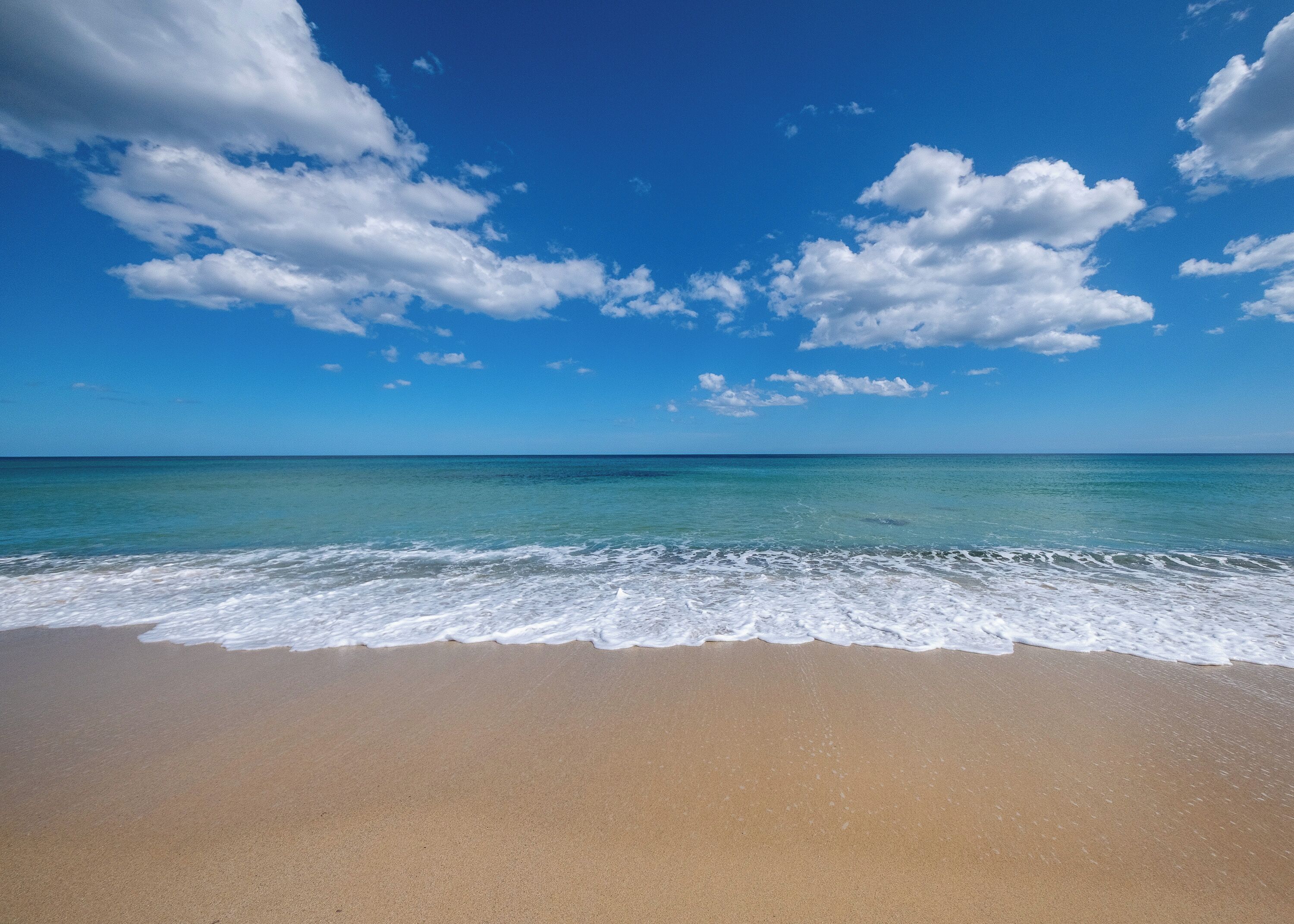 Une plage avec une eau d’un bleu limpide et un rivage sablonneux.