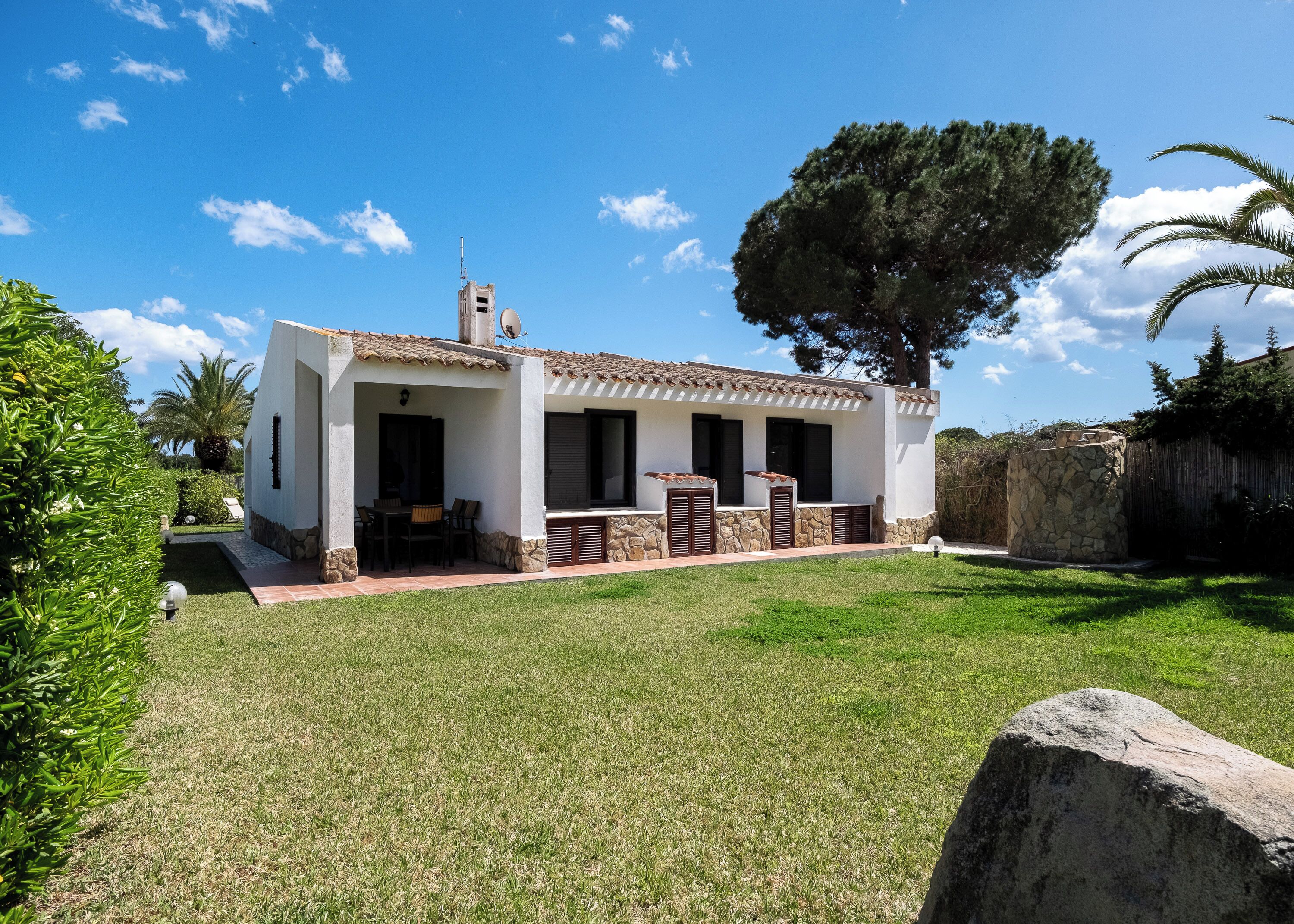 Una casa de un piso con patio, chimenea de piedra y un árbol grande en el jardín.