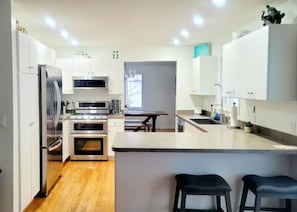 Uma cozinha moderna com armários brancos, eletrodomésticos de aço inoxidável e uma ilha central com banquetas.