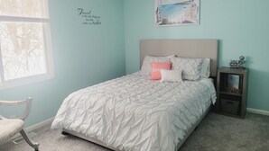 A bedroom with a bed, a nightstand, a chair, a window, and a wall with a quote.