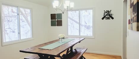 Un espace repas avec une table et des bancs en bois, de grandes fenêtres et un lustre.