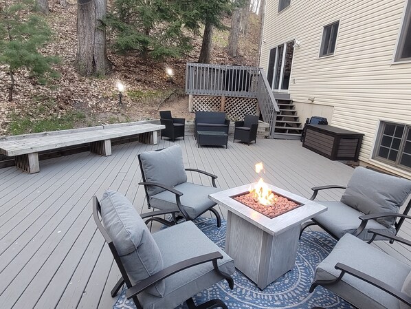 A deck with outdoor furniture, a fire pit, and a staircase leading to a house.