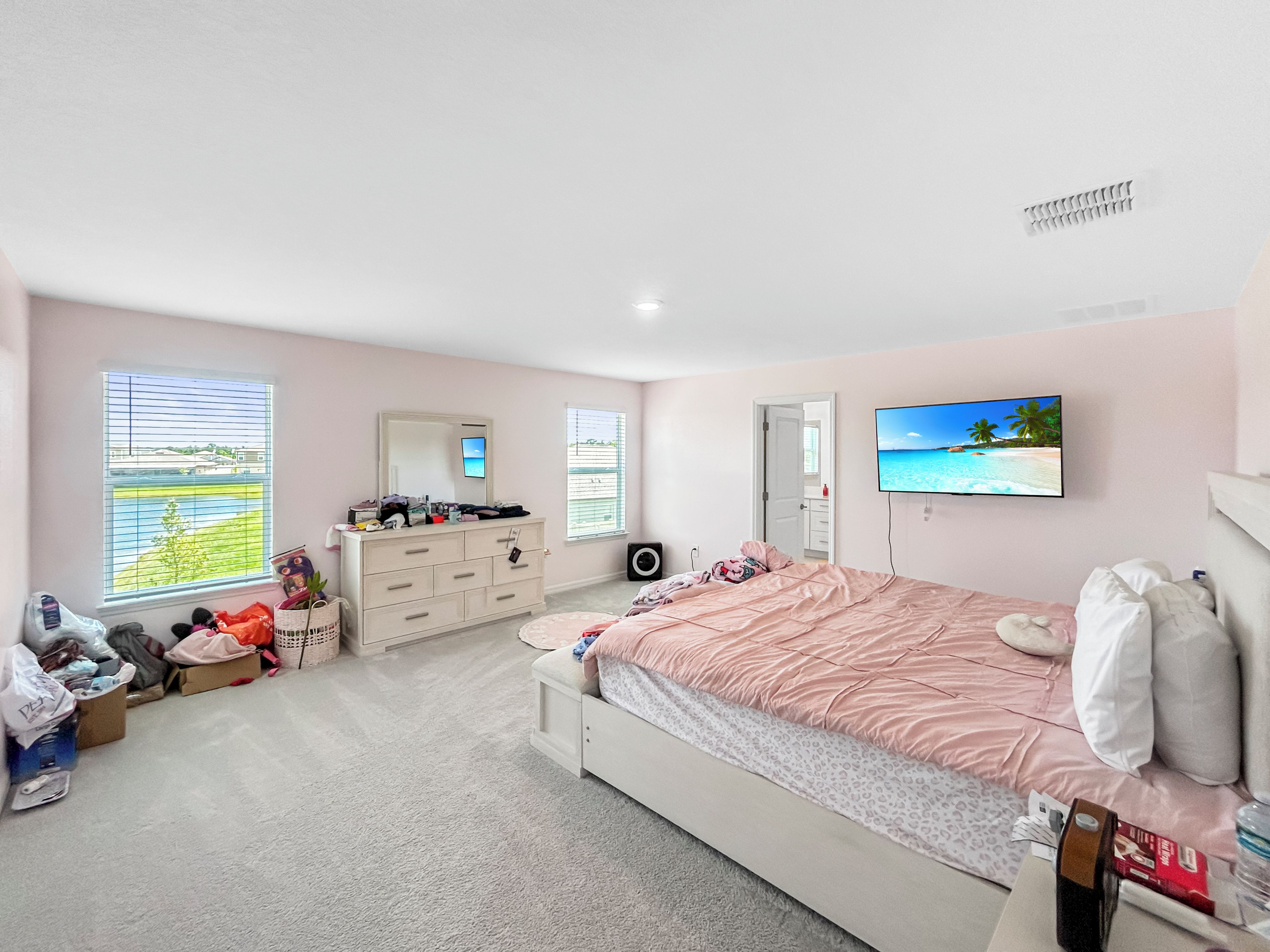 Ein Schlafzimmer mit Bett, Kommode, Fernseher und einem Fenster mit Jalousien.