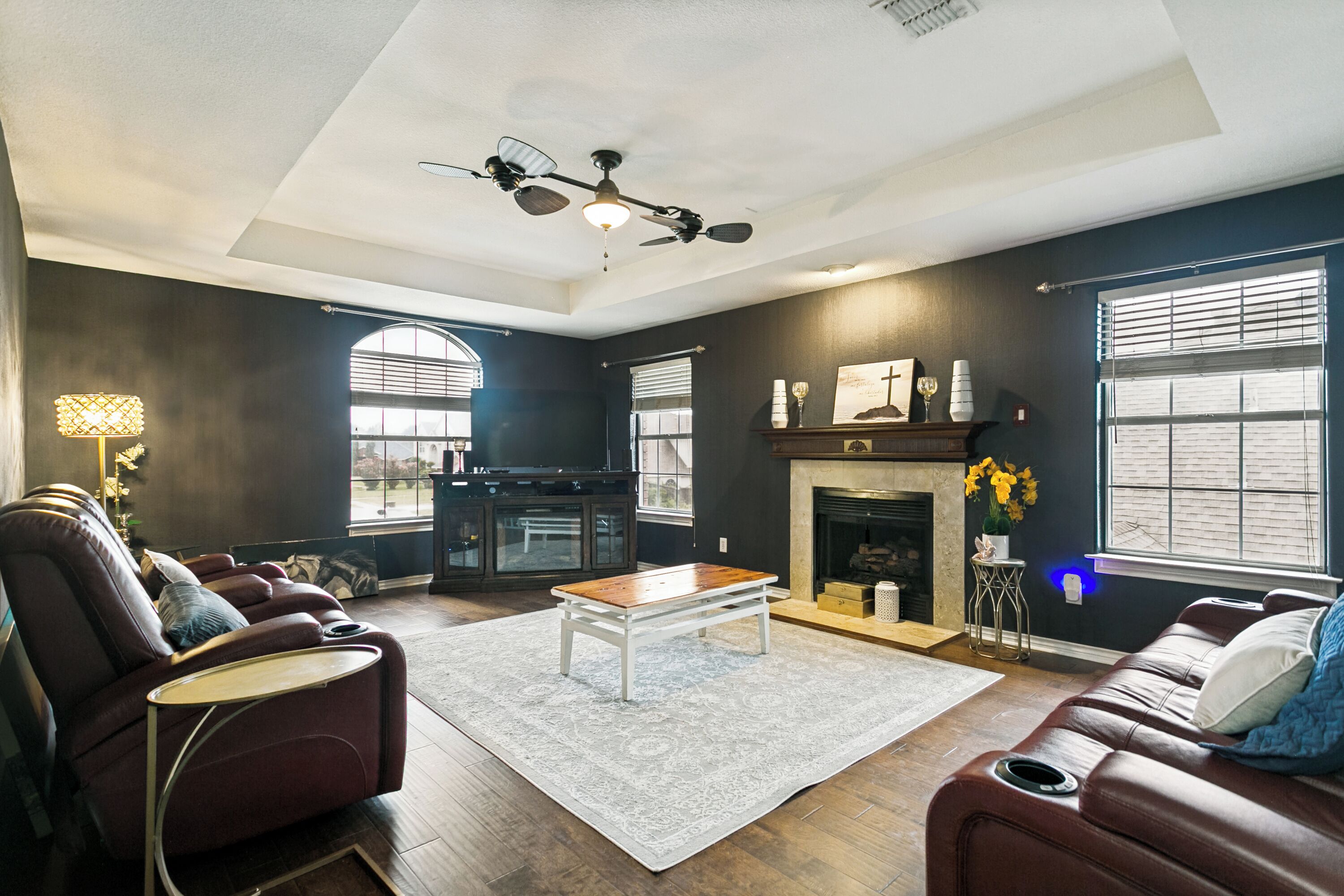A modern living room with a fireplace, leather sofas, a coffee table, and a ceiling fan.