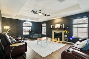 Ein modernes Wohnzimmer mit Kamin, Ledersofas, einem Couchtisch und einem Deckenventilator.