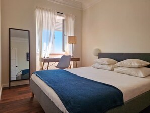 Une chambre d’hôtel avec un lit, un bureau, une chaise, une lampe et une fenêtre avec des rideaux.