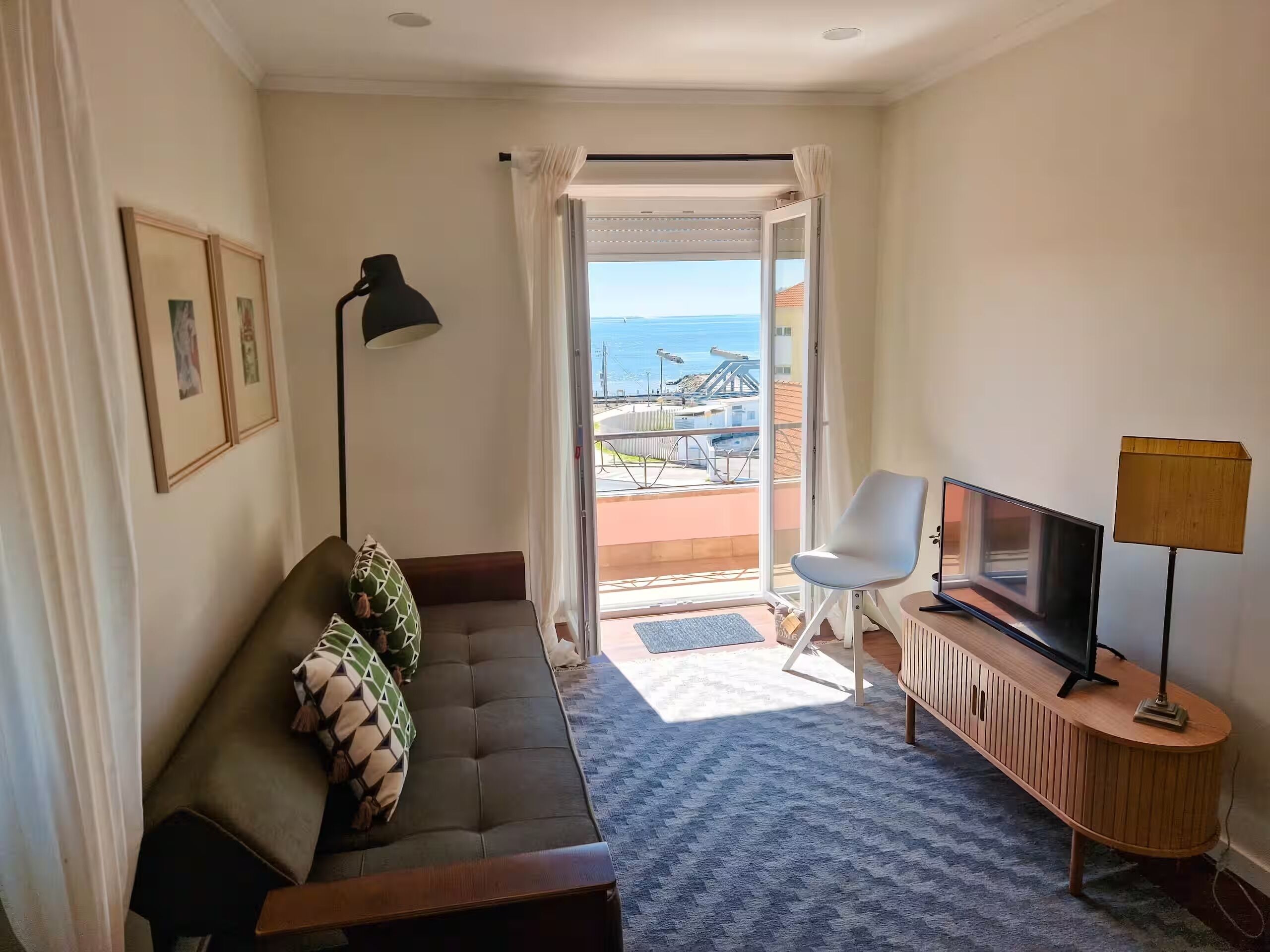 Een hotelkamer met een bank, een televisie, een lamp en uitzicht op de zee door een open deur.