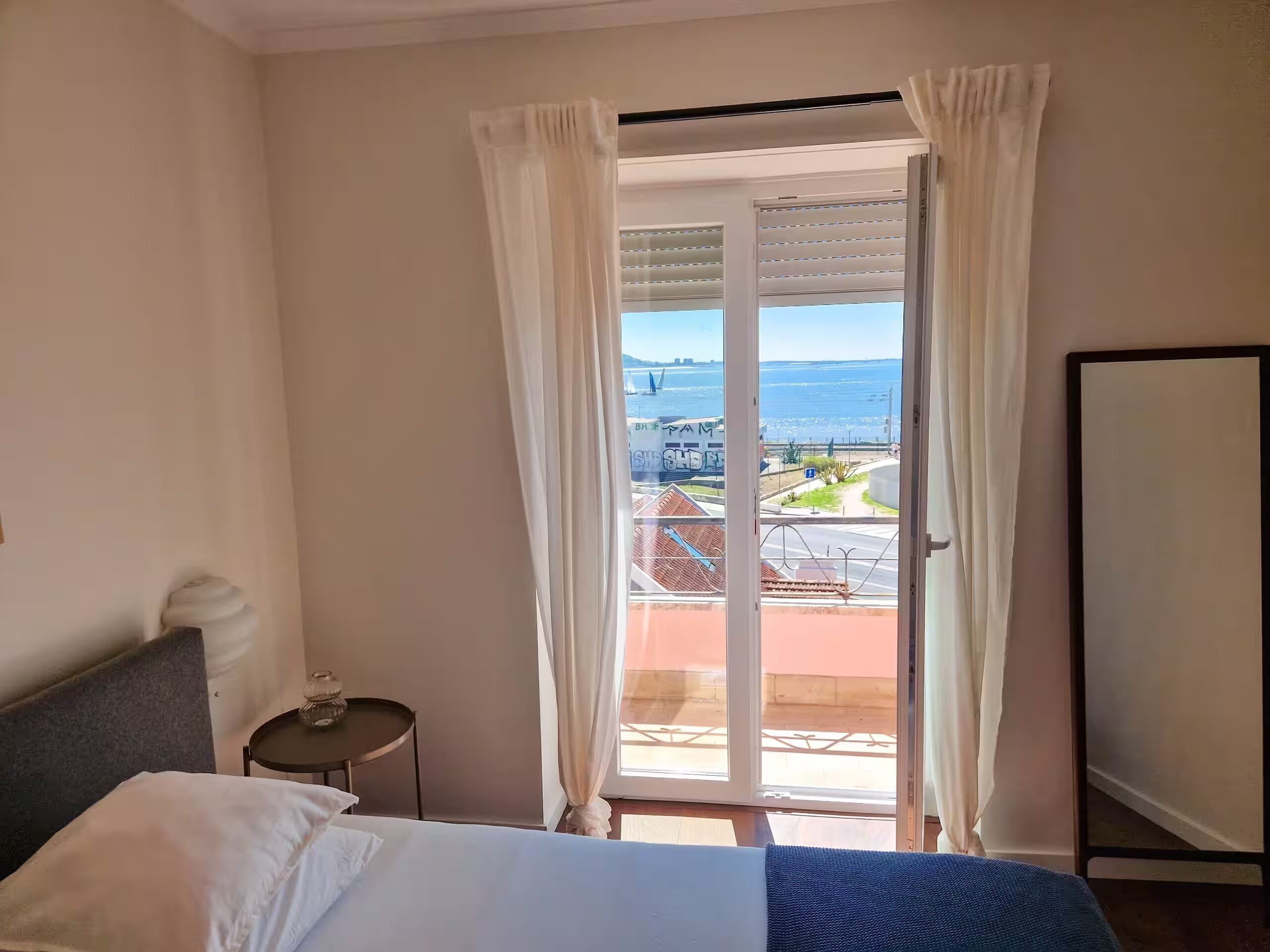 A hotel room with a bed, a small table, and a view of the sea through a sliding door.