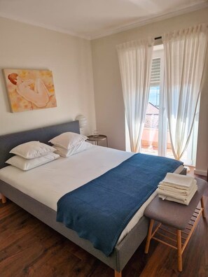Ein Hotelzimmer mit einem Bett, Kissen, einer blauen Decke, einem Holzstuhl, einem kleinen Tisch mit einem Glas und einem Bild an der Wand.
