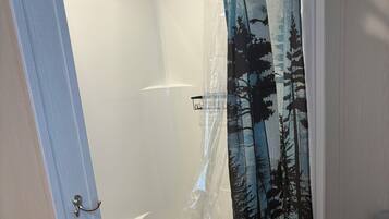 A bathroom with a shower curtain featuring a forest print, a white bathtub, and a wooden floor.