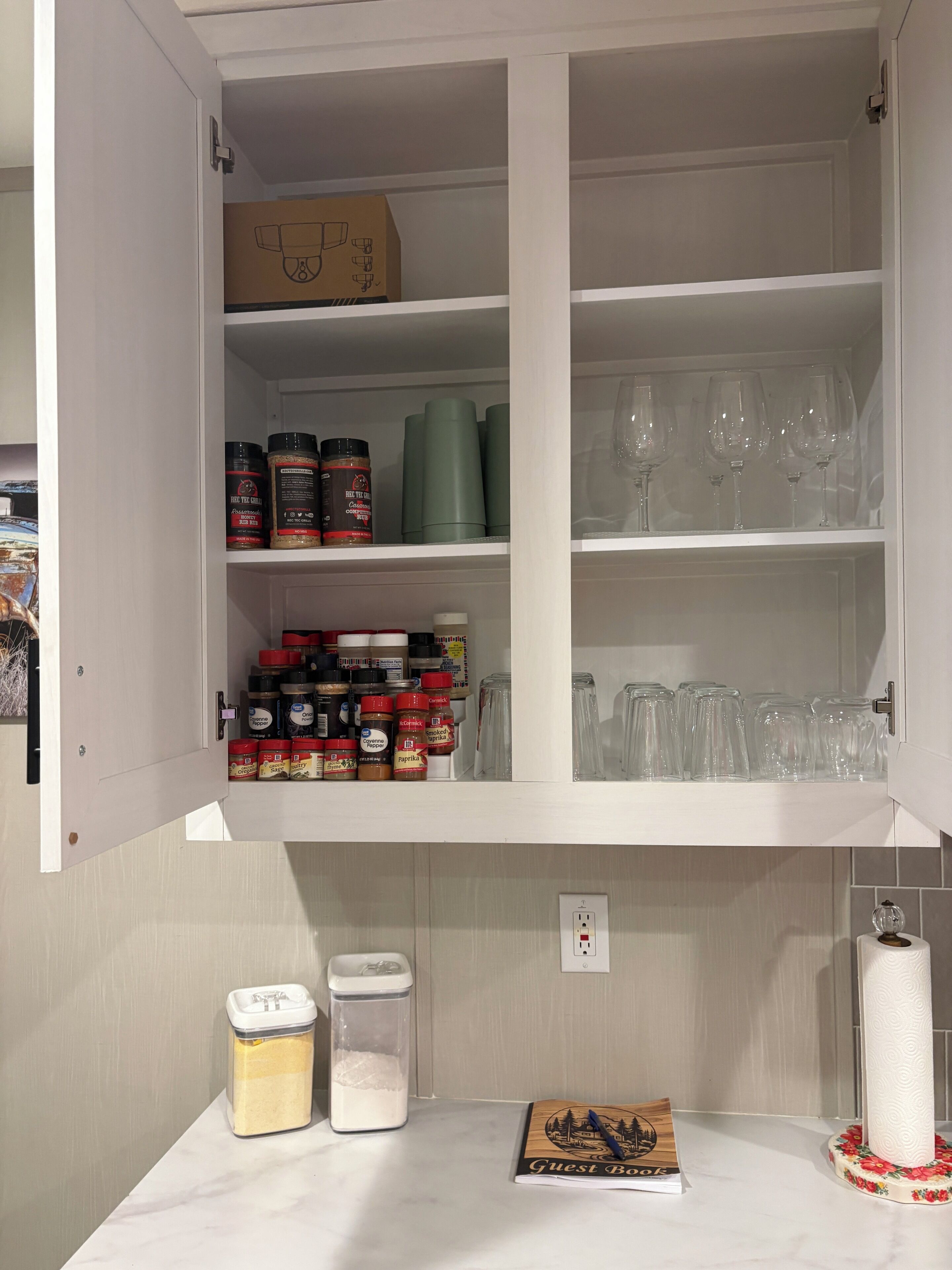 Un meuble de cuisine doté d’étagères où sont rangés des bocaux d’épices, une boîte et un rouleau d’essuie-tout.