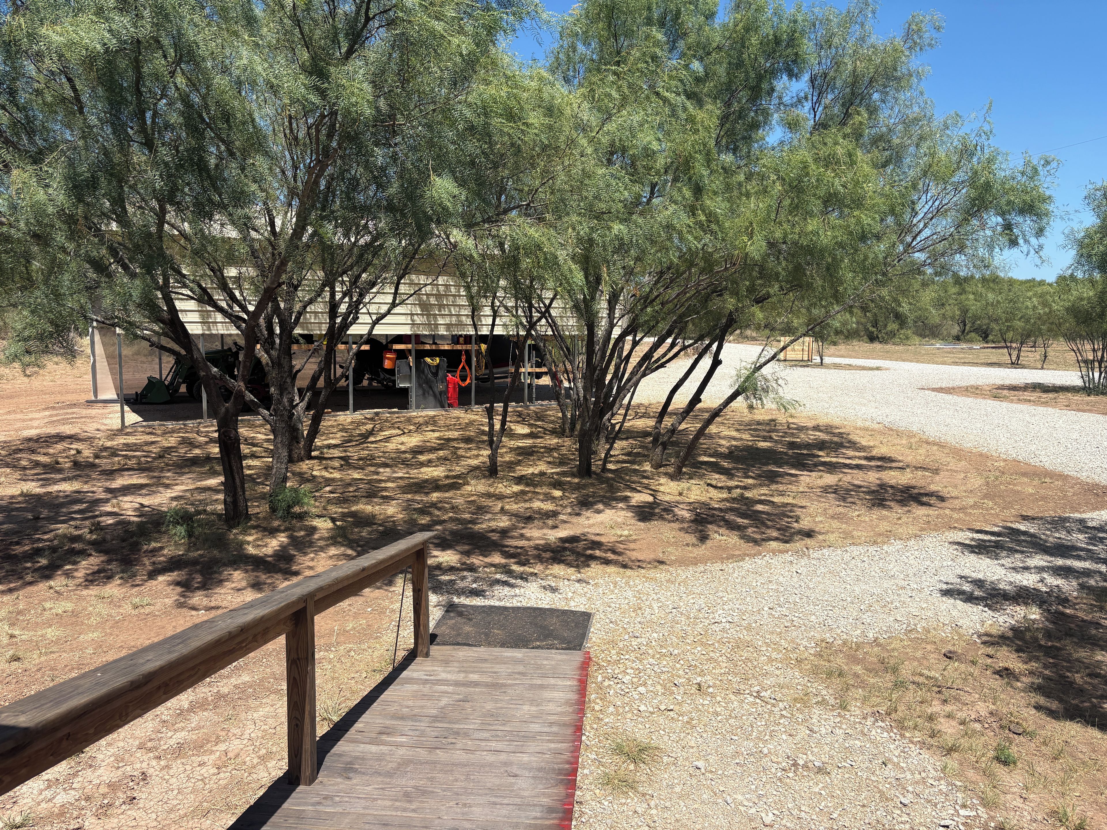 A wooden deck leading to a building with a covered entrance, surrounded by trees and a gravel path.