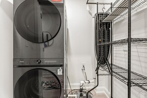A laundry room with stacked washing machines and a metal rack with pipes. - Modern 2BR DC Stay near Union Market, NoMa & H Street (Washington)