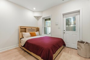 A bedroom with a bed, a window, a door, and a trash bin. - Modern 2BR DC Stay near Union Market, NoMa & H Street (Washington)