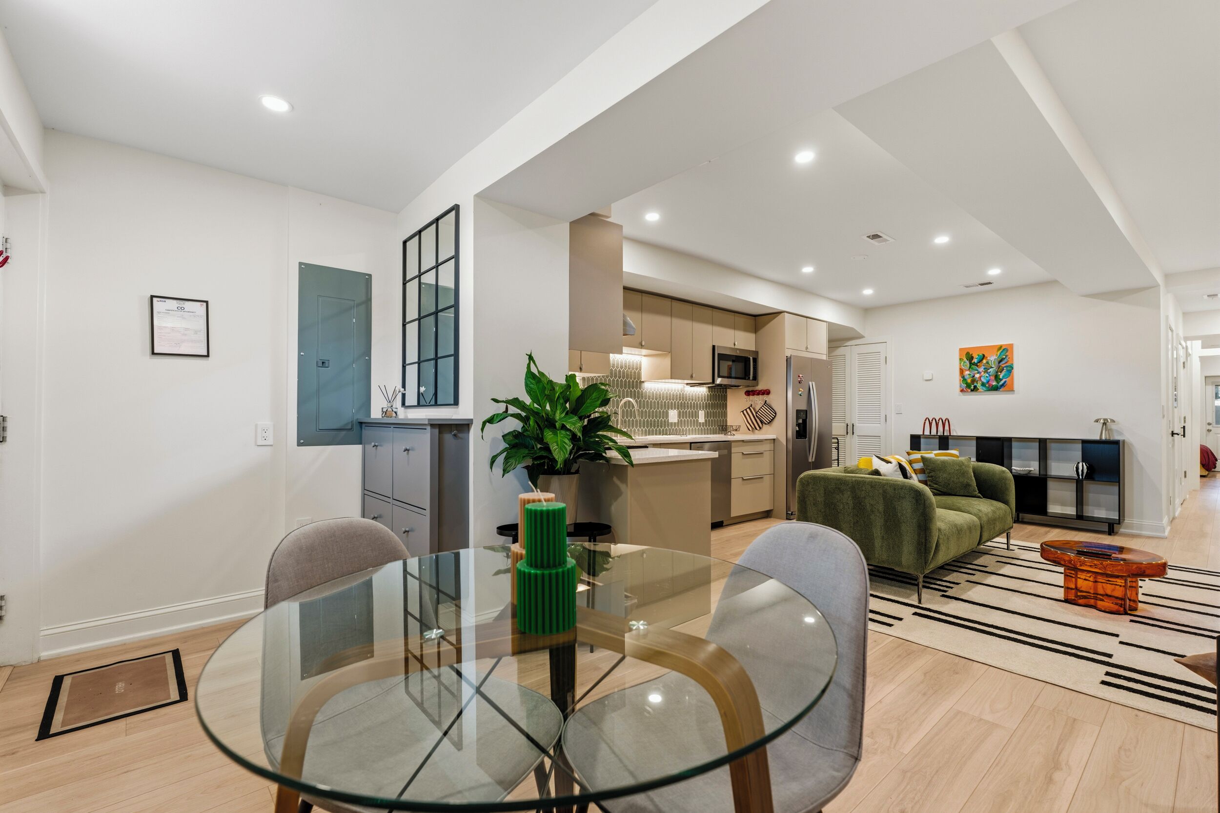 A modern living space with a glass dining table, a green sofa, and a kitchen area with a microwave.